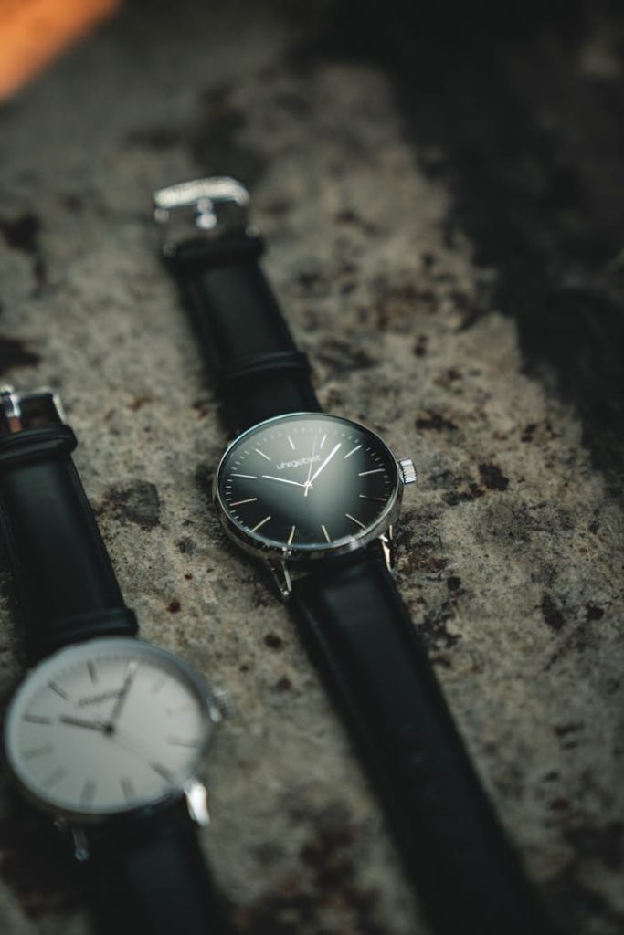 Photo of Two Analog Watches with Black Leather Bands on Gray Surface